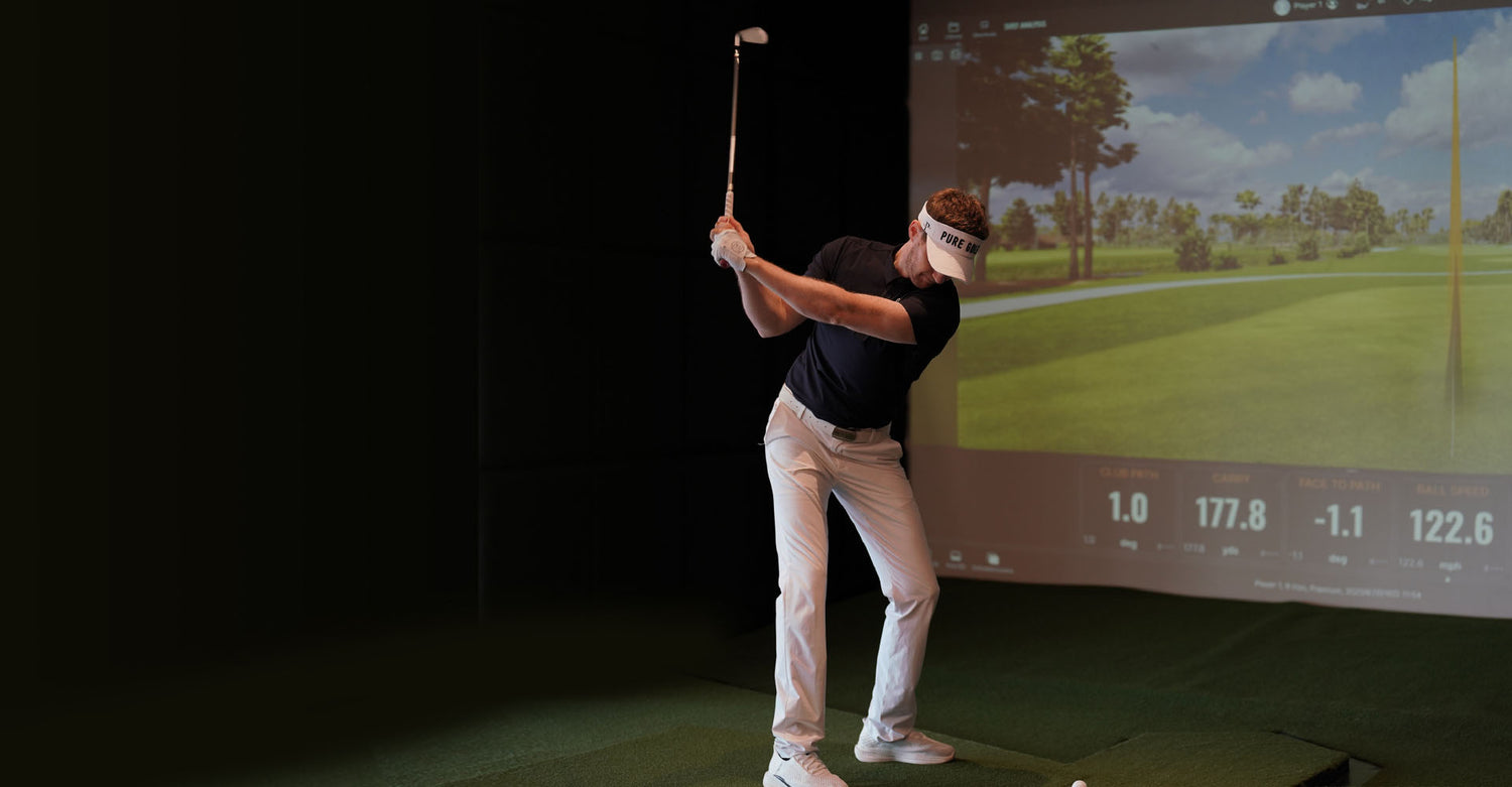 Coach Adam playing golf on a simulator with a screen displaying a golf course.